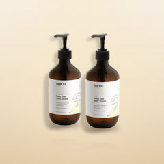 nureo Cedar and Cardamom Hand and Body Wash bundle, two amber pump bottles on warm golden studio background