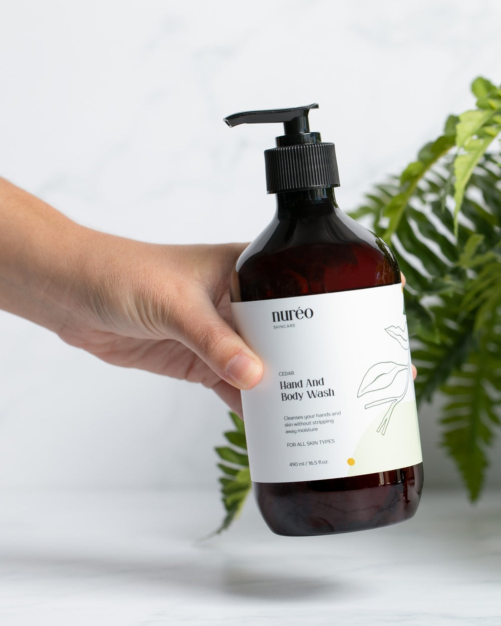nuréo Cedar Hand and Body Wash, 490ml, held to show scale