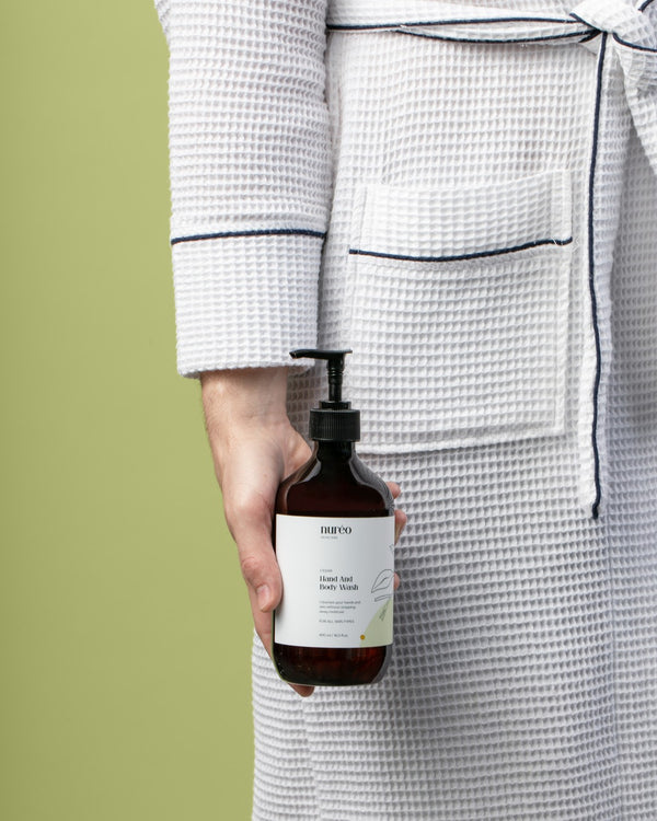 nuréo Cedar Hand and Body Wash held at the hip in a waffle robe