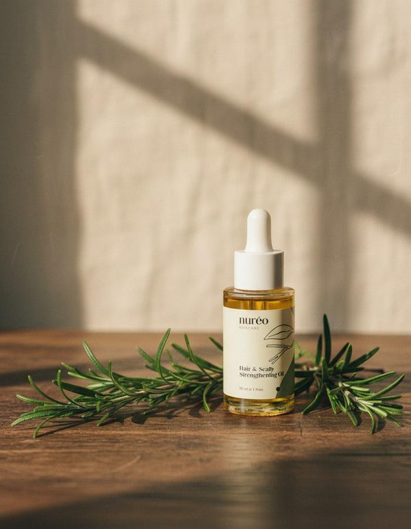 nureo Rosemary Hair Oil on walnut wood with fresh rosemary